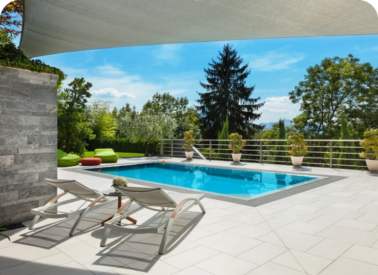 Outdoor pool with lounge chairs and trees.